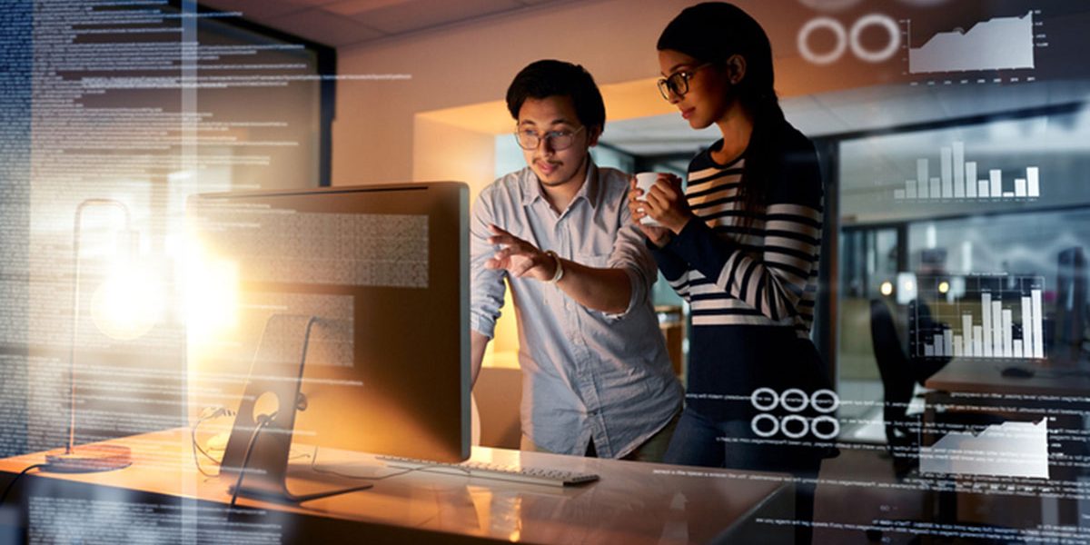 Two adults looking at a computer screen pointing with a cup of coffee.