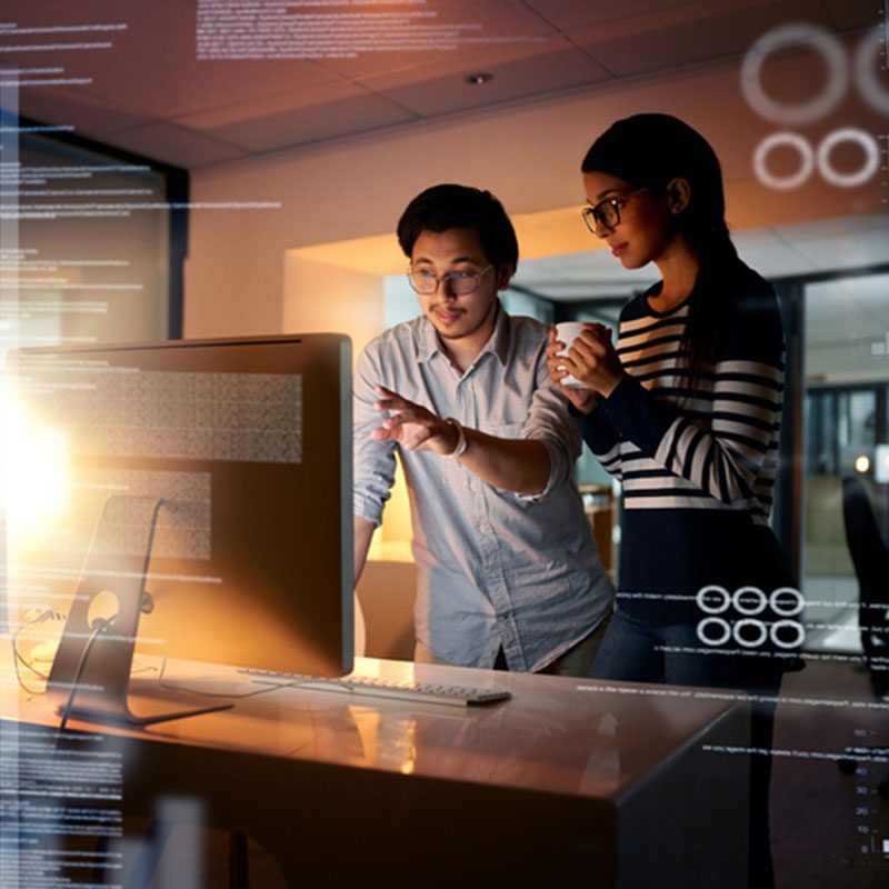 Two adults looking at a computer screen pointing with a cup of coffee.