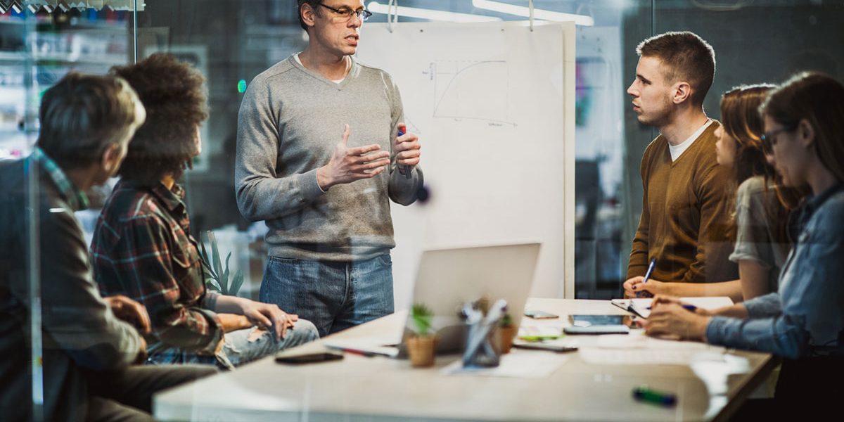 Marketing team standing in front of white board talking.