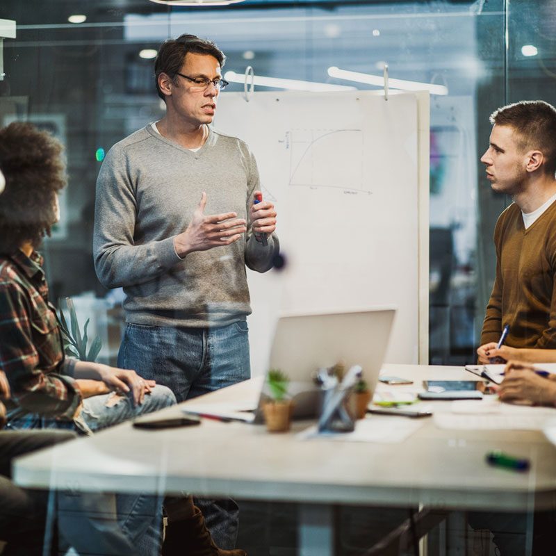 Marketing team standing in front of white board talking.