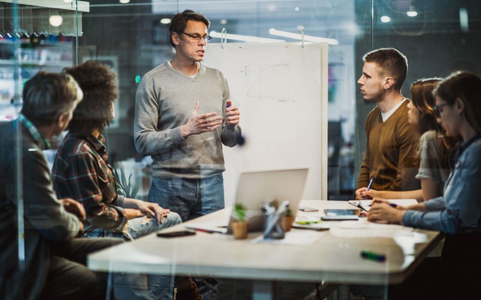 Marketing team standing in front of white board talking.
