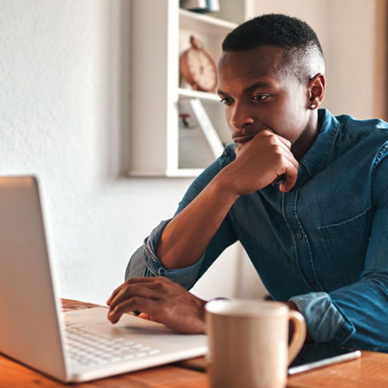 Black man reading laptop with cup of coffee.